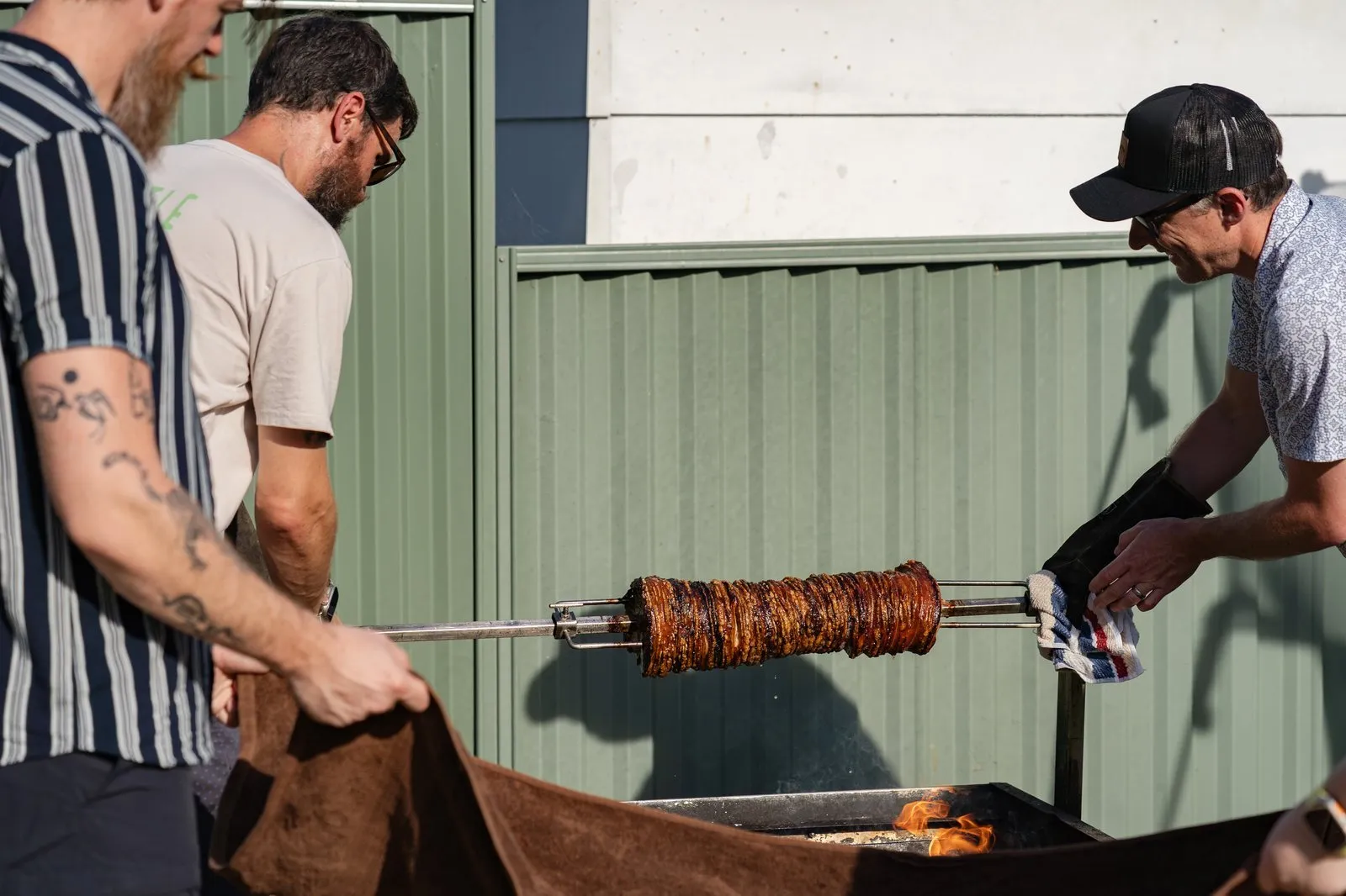 Two people cooking meat on a spit roast at a backyard cookout